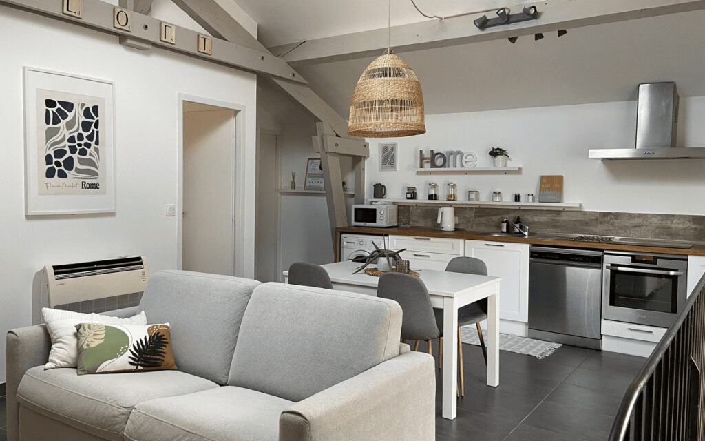 Salon avec canapé gris confortable donnant sur la cuisine américaine entièrement équipée.