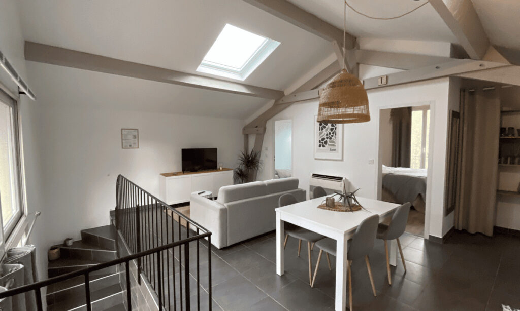 Pièce à vivre lumineuse sous les toits avec climatisation, espace repas et coin salon.