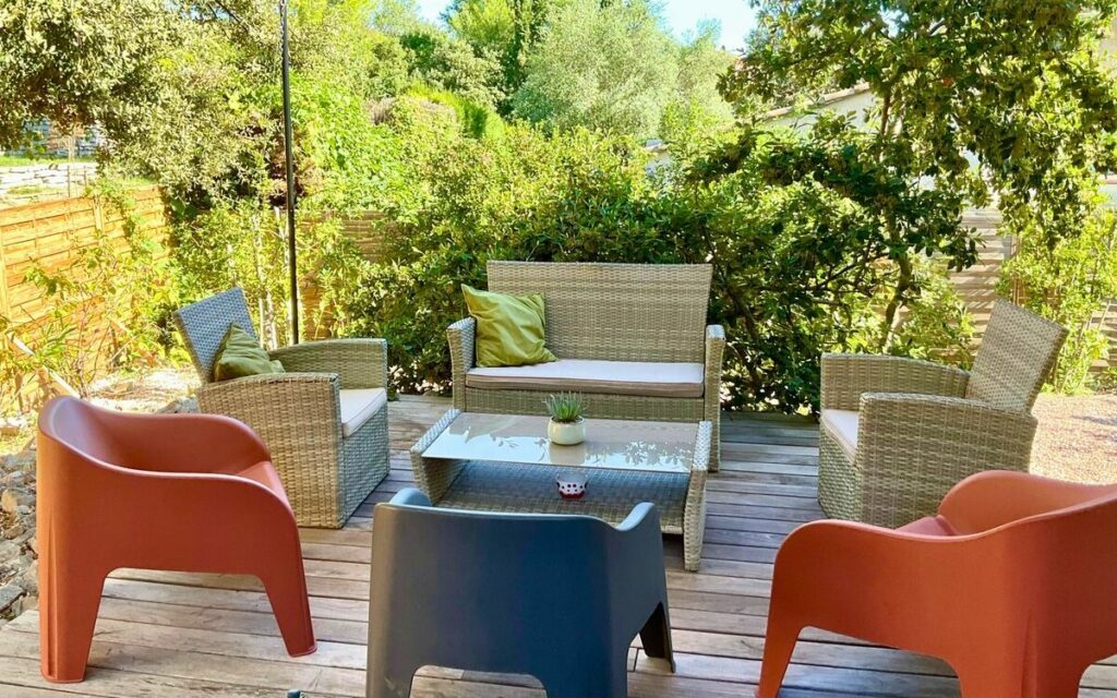 Grande terrasse en bois avec salon de jardin confortable entourée de verdure pour les repas en extérieur.